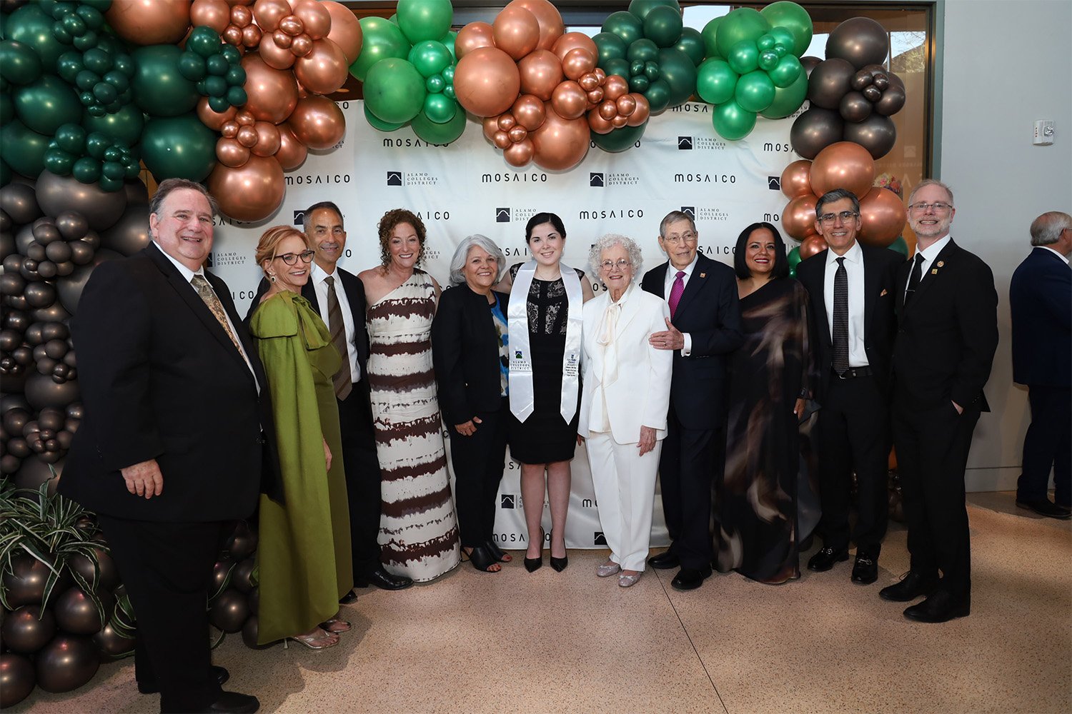 group of people standing in front of balloon arch dressed for gala