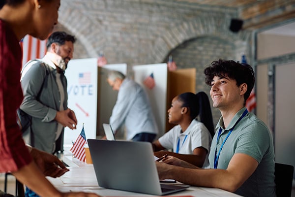 young man and woman smiling and assisting people voting at a polling site