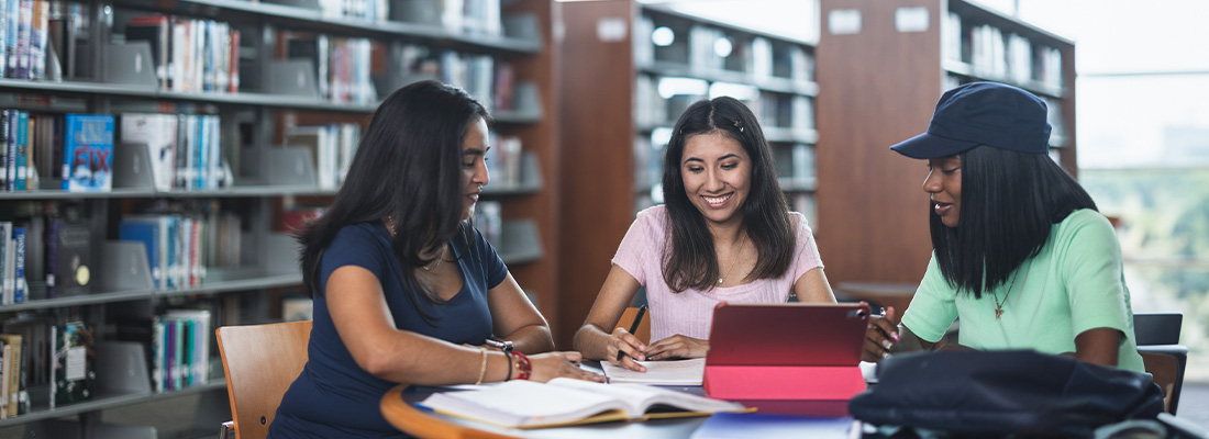 three female students sitting at a table in a college library