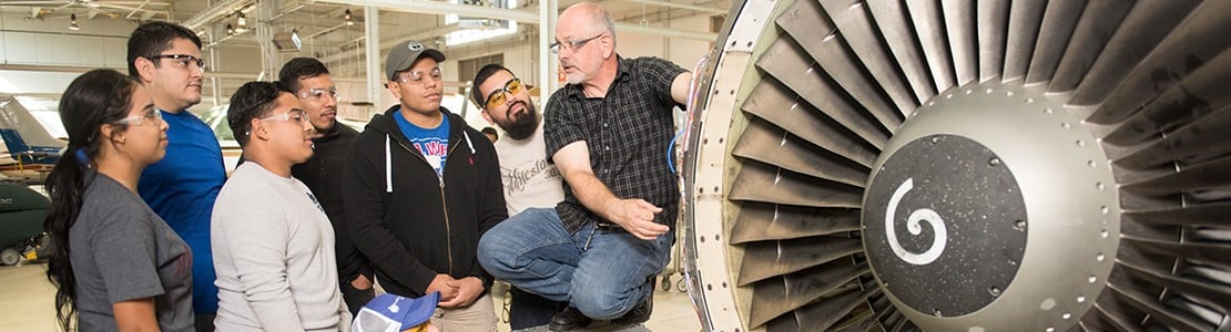 Students listening to professor next to an aircraft part