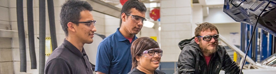 Students with safety goggles smiling next to a vehicle